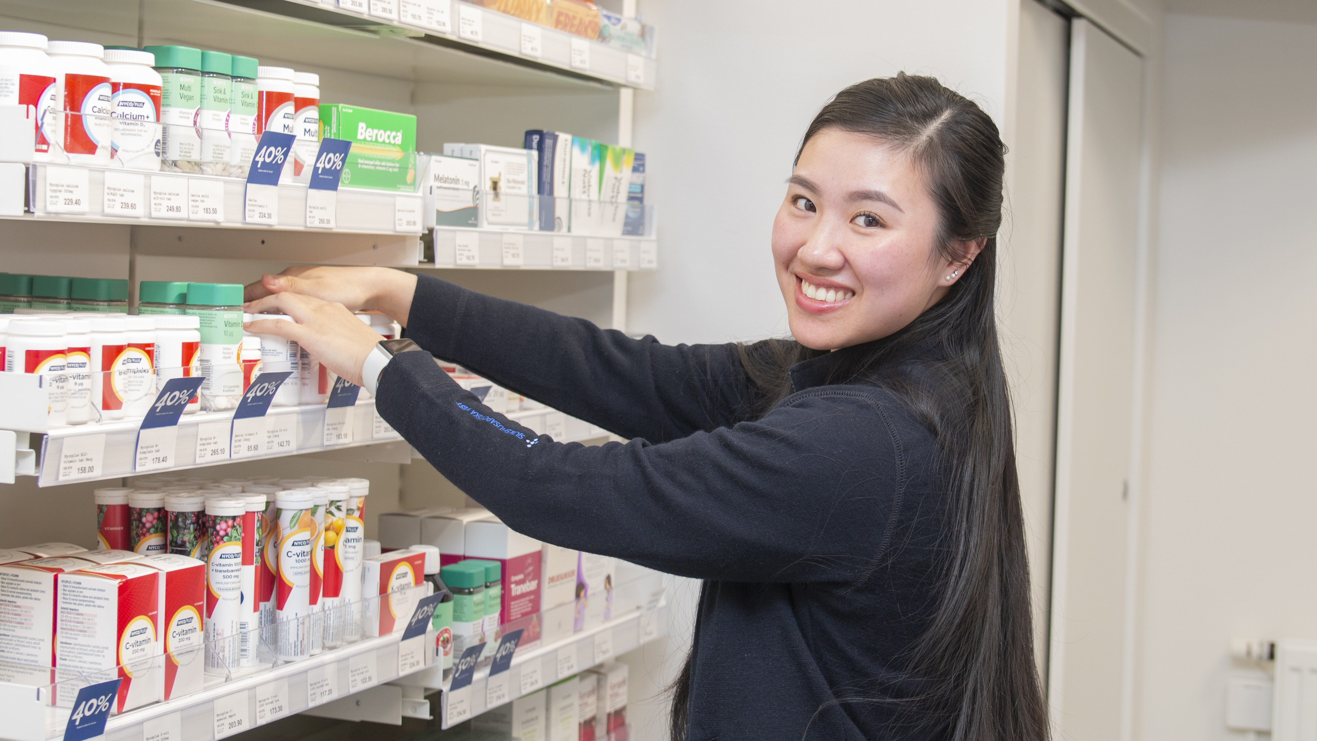 Thiet rydder i hyllene mens hun ser på kamera og smiler