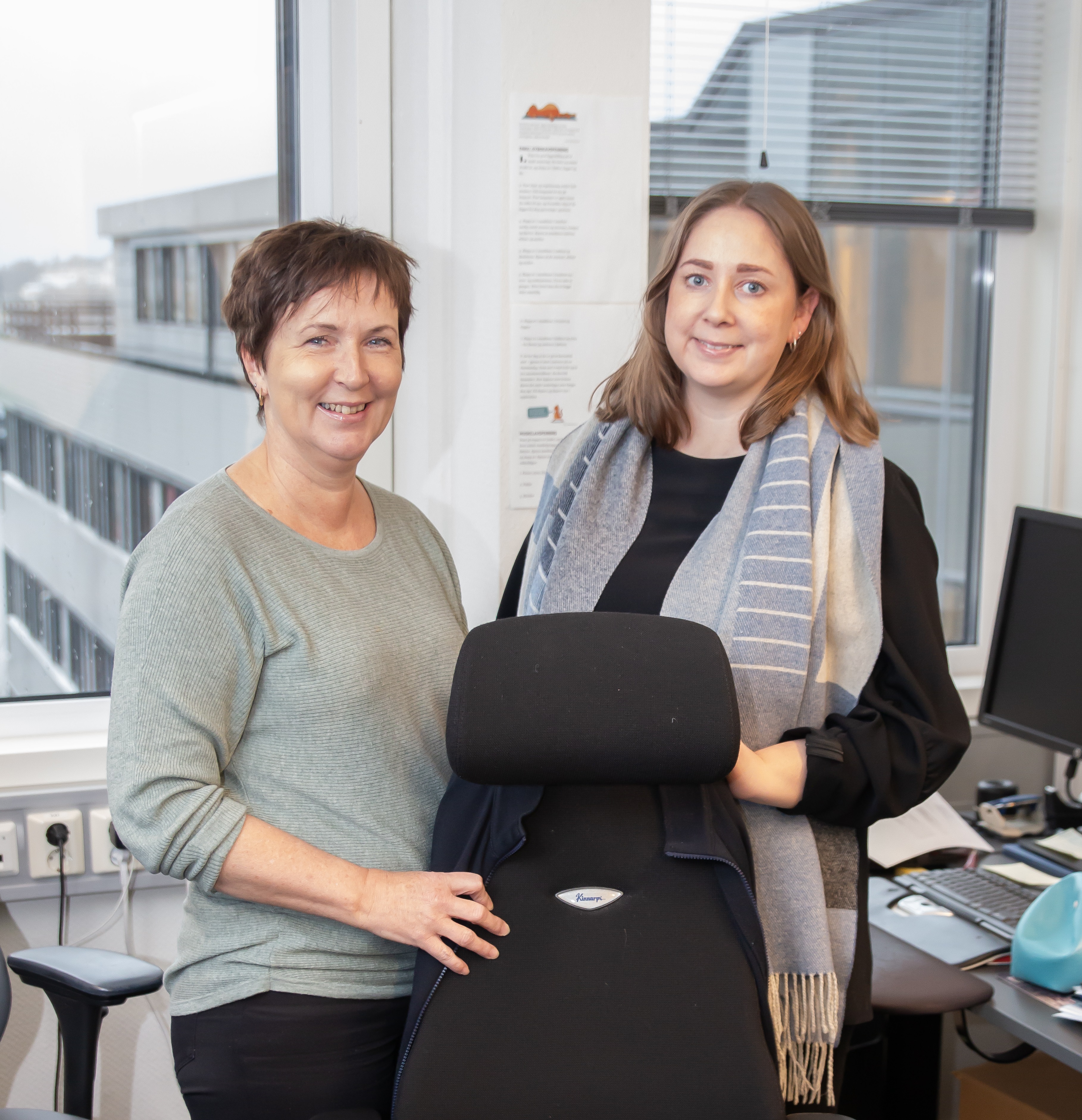 To damer i HR-avdelingen står ved siden av en tom kontorstol.