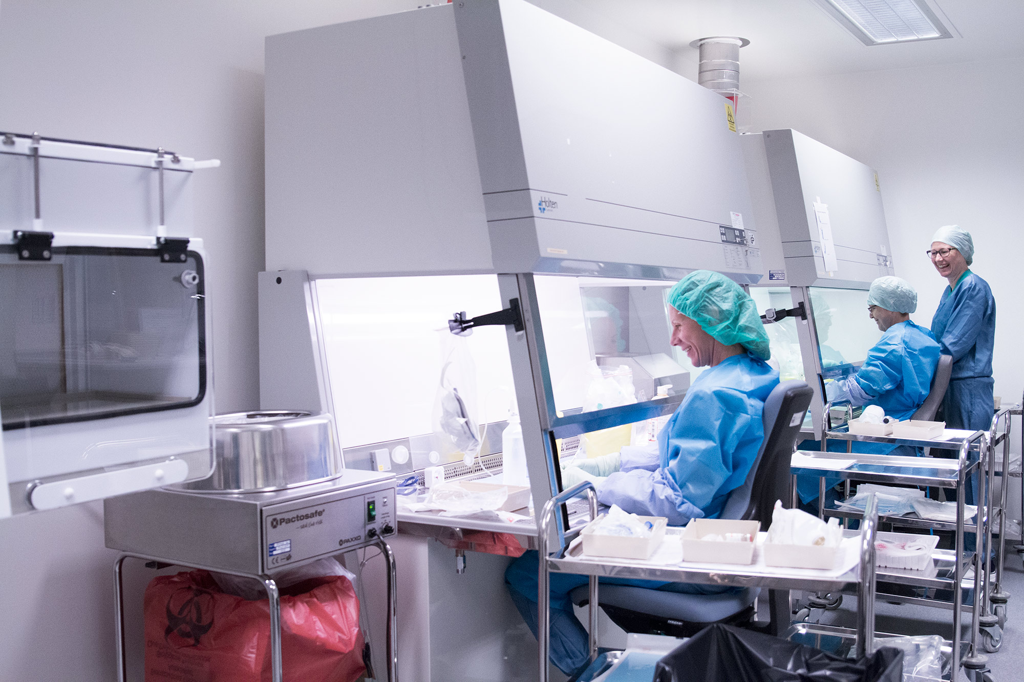 Apotekteknikere sitter og jobber i isolatorer med produksjon av legemidler.