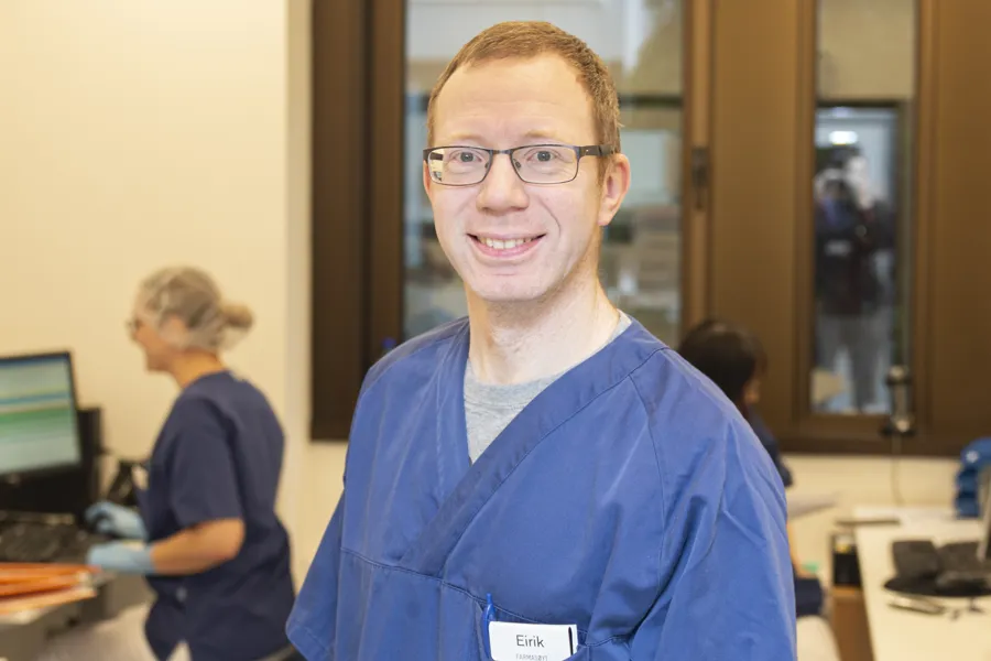 Eirik Svandal smiler til kamera mens en kollega jobber ved PCen i bakgrunnen