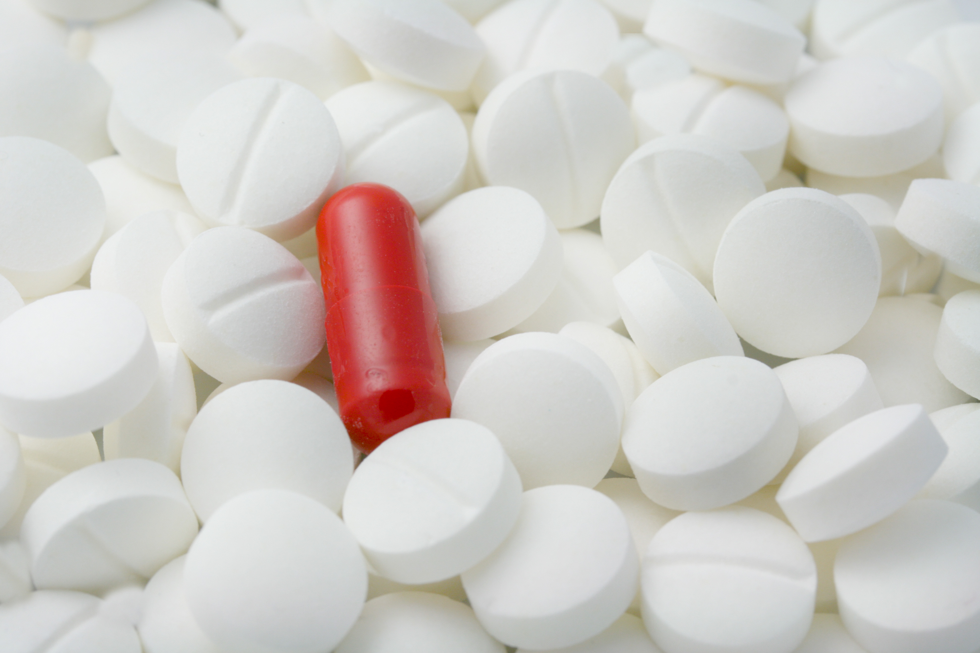En rød og hvit kapsel i en haug med piller