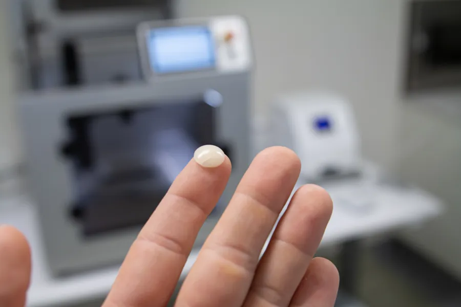 En hånd holder opp en geleklump med en 3d-printer i bakgrunnen.