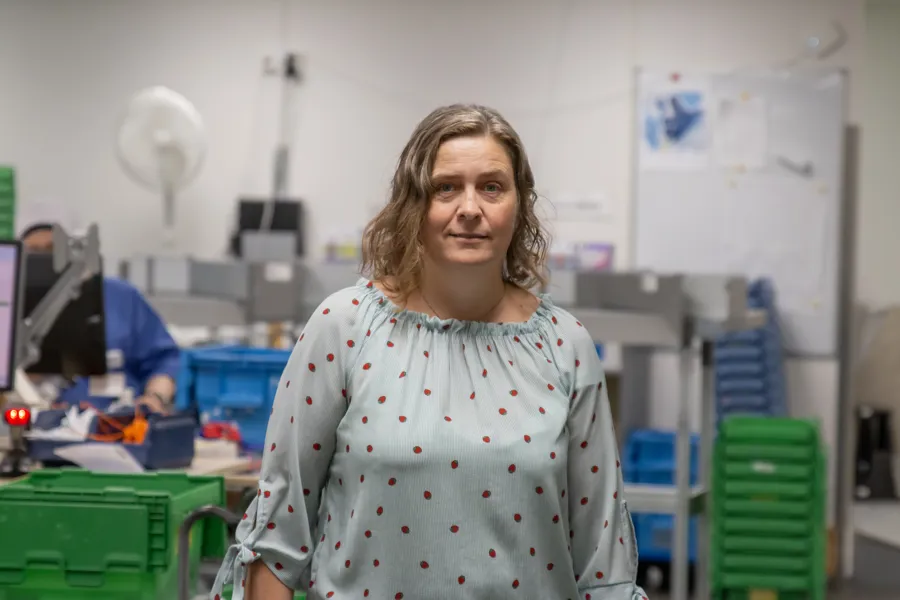 Trude står inne på sykehusekspedisjonen hvor man plukker medisiner som skal ut til sykehuset og smiler skakt til kamera.