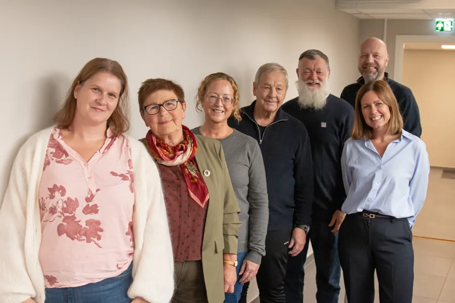 Brukerutvalget, som består av seks representanter står langs en hvit vegg. Administrerende direktør, Tonje Folkvang står ved siden av den bakerste.
