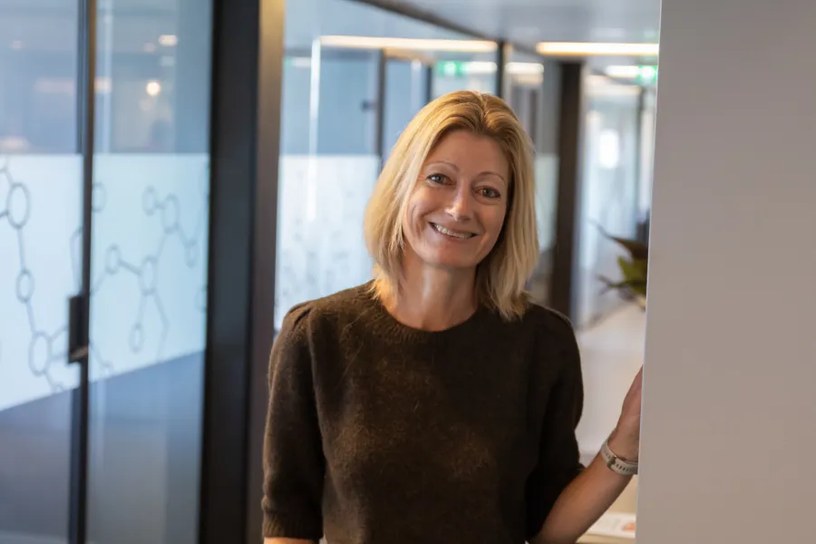 Linda står ved en vegg og lener seg inntil veggen mens hun smiler til kamera