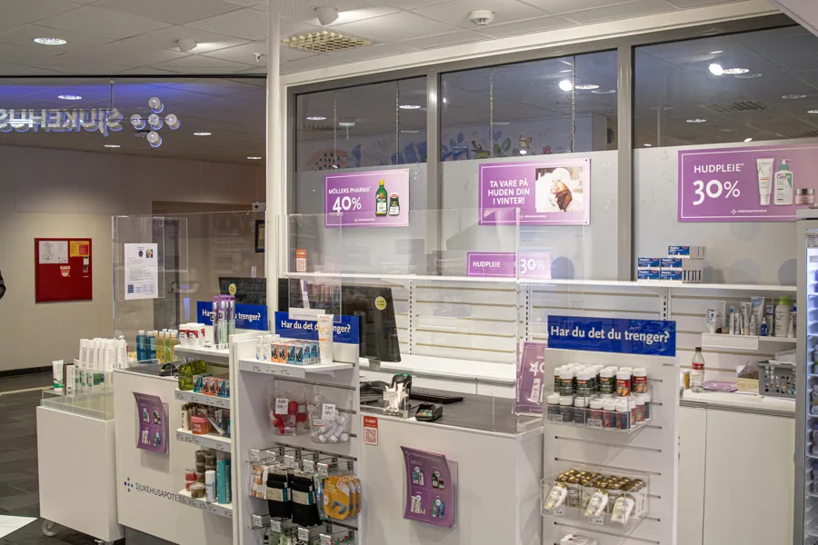 Apoteket ved sykehuset i Stavanger sett utenfra. Det er lilla reklameplakater hengende fra taket for en kampanje som pågår.