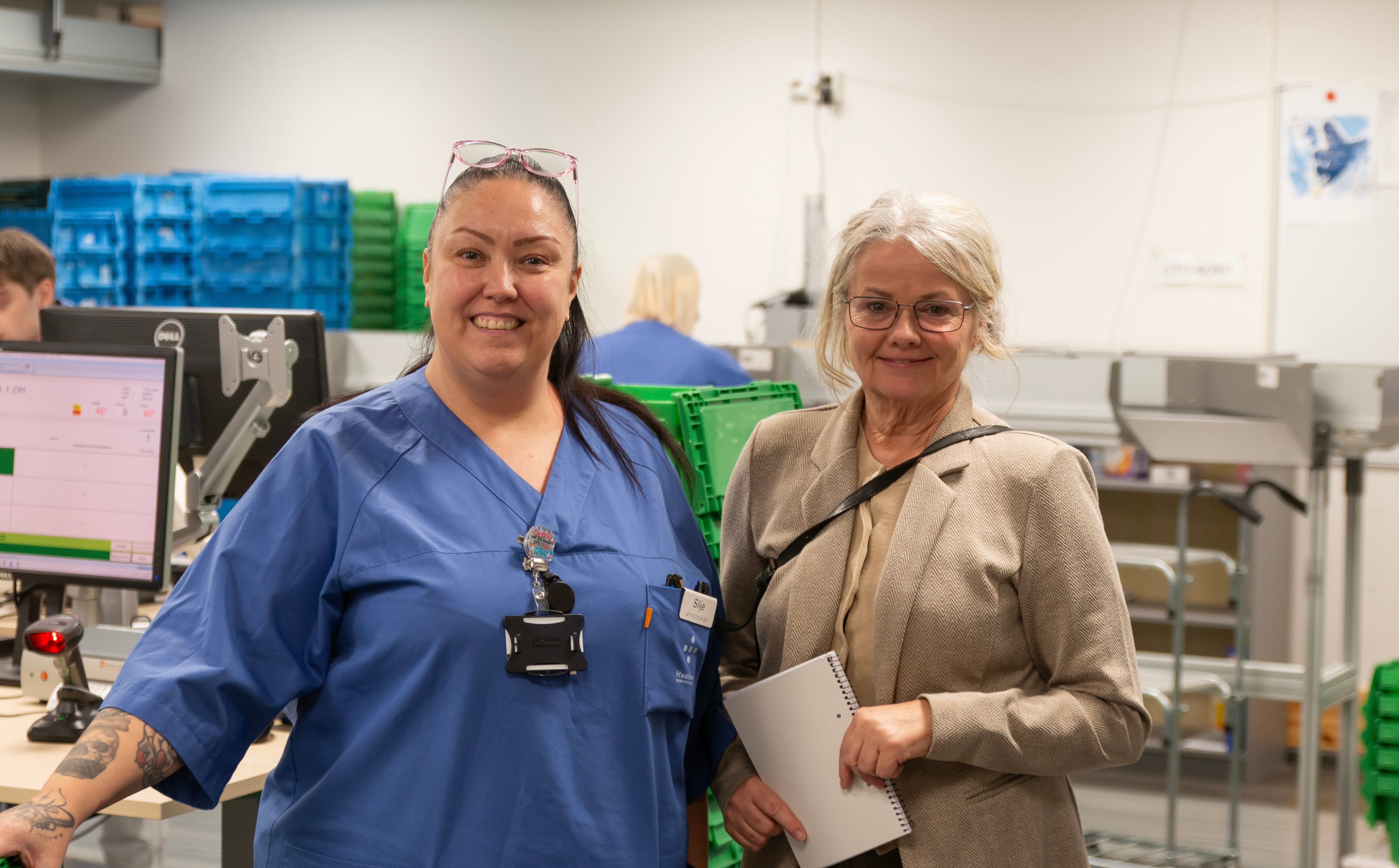 Silje Beuster og Tove Kittelsrud poserer for kamera foran plukkavdelingen på sykehusapoteket i Bergen.